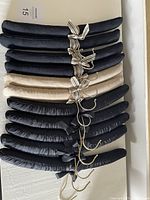 Top view of all 11 velvet hangers stacked together. 5 solid black velvet hangers, 2 beige velvet hangers with striped ribbons, 4 black velvet hangers with striped ribbons.