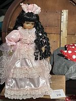 Full view of the vintage porcelain doll in her pink ruffled satin and lace ball gown standing on a wooden flat base.