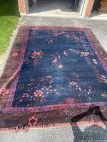 Full view of rug laid out on driveway showing overall dimensions, central navy blue field, magenta and brown borders