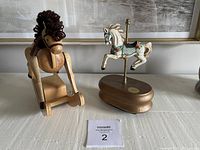 Wooden rocking horse and carousel horse music box displayed side by side on a white surface against a light wall background.