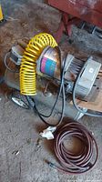 Full view of Campbell Hausfeld PowerPal air compressor tank, attached yellow coiled hose, and additional brown hose on the floor.