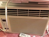 Front view of GoldStar window air conditioner unit with remote control placed in front.