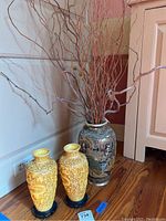 The two smaller yellow vases with dragon relief carvings and one larger Asian vase with painted decoration and branches, placed on wooden floor.