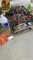 Overall image showing assembled lot items including hydraulic jack, jumper cables, battery chargers, fluids, and straps.