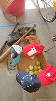 Wide shot showing lot contents including bats, gloves, hats, and a box of balls