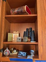 Wide view of cabinet shelf displaying the leather case, binoculars, lighters, flask, and opera glasses.