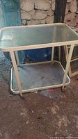 Full view of metal cart showing glass top surface and metal bottom shelf on wheels in a basement setting