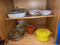 Cabinet shelf holding multiple baking dishes, cookware including yellow Dansk metal pot and glass baking dishes