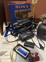 Sony Handycam Vision Video8 digital camcorder with box, charger, battery, manual, cassette boom box, cassette recorder, telephones, and cassettes visible.