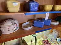 Shelf view showing blue Hall Refrigerator Ware lidded dishes, porcelain lidded dish and floral platter on wooden shelf.