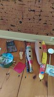 View of all instruments arranged on wooden floor including flute, shakers, drum, kalimba, jaw harp, plucker, and percussion tool.