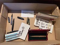 Ten pens and pencils laid out in a box including various fountain pens, Cross brand items in boxes, and notes describing gold fillers and items.
