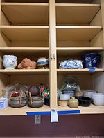 Wide shot showing multiple planters and pots displayed on wooden shelves including baskets, ceramic pots in white and brown, Delft planter and miscellaneous small items in plastic bags.