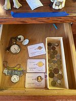 Drawer top view showing two pocket watches on the left and plastic card medallions with assorted coins on the right