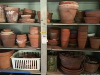 Shelves filled with assorted terra cotta pots and matching saucers, some painted and showing white residue and wear.
