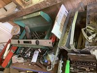 Overview photo showing green metal toolbox, sockets, hand tools, and levels stacked on a surface among other tools.
