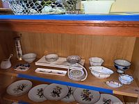Shelf display with assorted vintage porcelain bowls and plates including floral designs, pierced blue and white bowl, and large rectangular plastic plates.