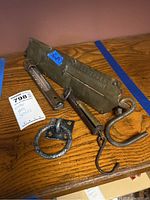 Photo showing the full brass hanging scale with hooks lying on a wooden surface, accompanied by a metal ring piece.