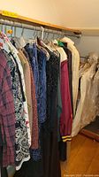 Photo of various women's dresses, shirts, and jackets hanging from a clothes rack showing different colors and fabric types including heavily used items.