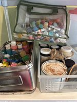 Photo showing multiple containers filled with a variety of small paint bottles and jars, brushes, and wrapped canvases.