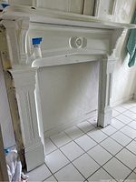 Front view of the white wooden fireplace surround frame placed against a wall on tiled floor.