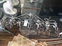 Two metal hanging wall racks with decorative scroll and flower details, each with five hooks, displayed on a dark surface with surrounding household items.