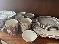 Variety of china including mugs with floral designs, salad plates, and small cups.
