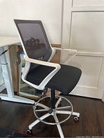 Side angle view showing white frame, black mesh back, cushioned seat, chrome foot ring and caster base