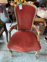 Front view of velvet and wood occasional armchair showing red-orange fabric and intricate wooden frame.