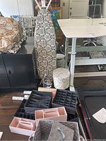 Photo showing ironing board with damask patterned cover, multiple drawer organizers in black and pink, woven basket and lids, small floral container, and rolled liners.