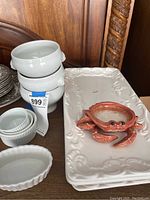 Photo shows a white ceramic platter with embossed decorative edges and a reddish-brown Fitz and Floyd crab-shaped dish on top, along with white ribbed soup bowls stacked.