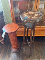 Pair of pedestals including a wooden cylindrical pedestal and a tall metal plant stand with distressed top.