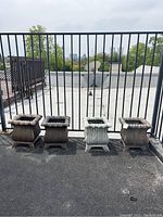Four resin planter pots displayed in a row near a black metal railing. Three are brown and one light gray.