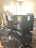 Sharp 44-inch flat screen TV with glossy black bezel, two remotes on black cabinet, cables coiled beside it