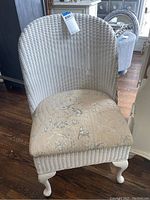 Front view showing the wicker chair with high curved back and floral upholstered seat.