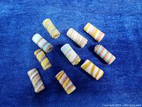 Ten cylindrical glass beads with multi-colored swirl patterns arranged on a blue fabric background.