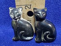 Two black cat-shaped miniature measuring tapes, one with paint wear and the other smooth black.