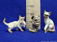 Front view of three vintage porcelain cat figurines with ruler showing size