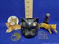 Lot of cat themed items including figurines, candle holder, and metal charms arranged near a ruler for size reference.