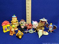 Lot of collectible vinyl figures including Garfield, Tasmanian Devil, Hello Kitty, red dragon, miniature house, wooden carriage, and various animal figures arranged with ruler for size reference.