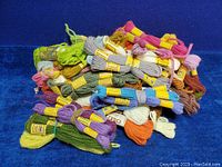 Several skeins of mixed color yarn piled on a blue background, showing variety of wool and polyester fibers with labels.