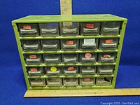 Front view of green Raaco metal storage organizer with all 25 labeled metal drawers closed. Rulers placed for size reference.