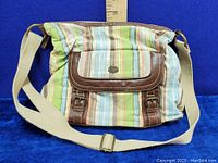 Front view of the fabric cross body bag showing multicolor pastel stripes, brown leather trim around front pocket, and cream adjustable strap