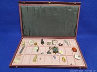 View of entire open display case with pink velvet lining and 20 small collectible items arranged in compartments.