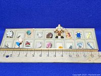 Display case with 15 small assorted trinkets placed on a blue background, ruler included for size scale.