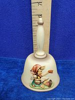 Full front view of the Goebel Hummel vintage 1979 porcelain bell showing shape, handle, and figurine on front.