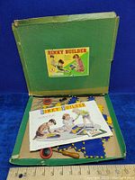 Photo showing open box with scattered blue and yellow interlocking plates, red wheels, wooden screwdriver and instruction booklets on top.