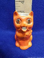 Front view of orange cat creamer showing detailed eyes, facial features, and spout opening.