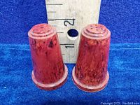 Front view of two reddish marbled Bakelite salt and pepper shakers, approximately 2 inches tall, with a ruler for size reference.