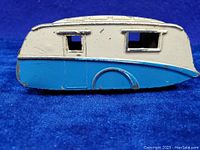 Side view of the vintage Dinky Toys die cast caravan trailer showing cream and blue painted body with window openings and paint wear
